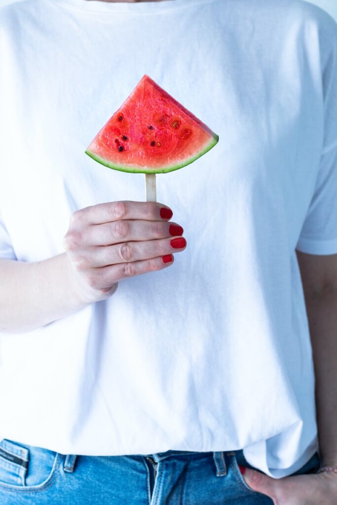 person in white crew neck t-shirt holding watermelon
